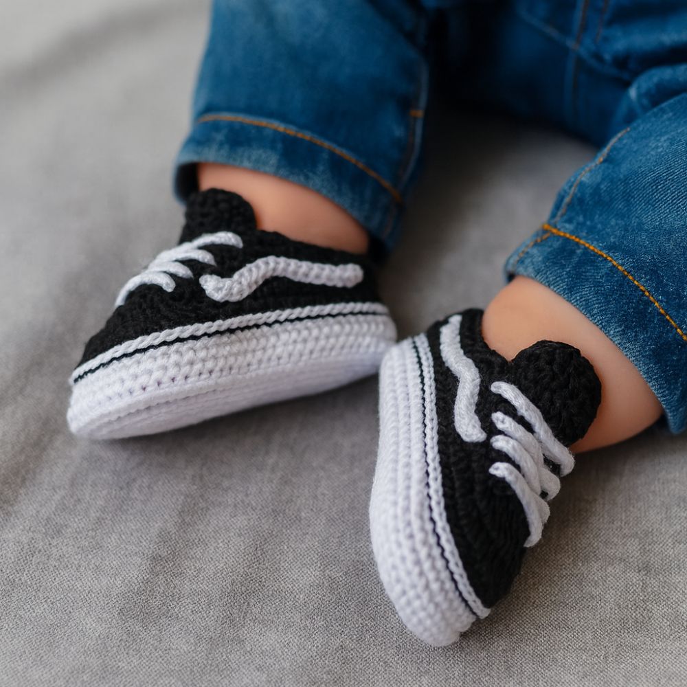 Black crochet baby sneakers with white sole worn by newborn in blue jeans — PDF pattern for handmade baby shoes