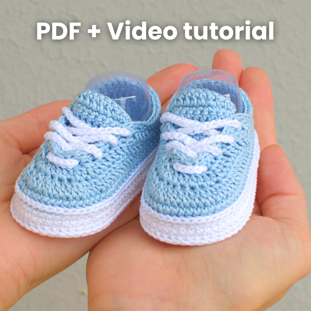 Pair of blue crochet baby sneakers in hands with text PDF + Video tutorial — crochet pattern and video guide