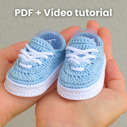 Pair of blue crochet baby sneakers in hands with text PDF + Video tutorial — crochet pattern and video guide
