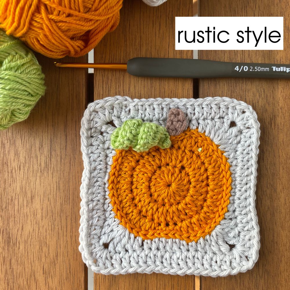 Rustic crochet pumpkin square in orange and gray with 3D leaves and stem, surrounded by warm-tone yarn