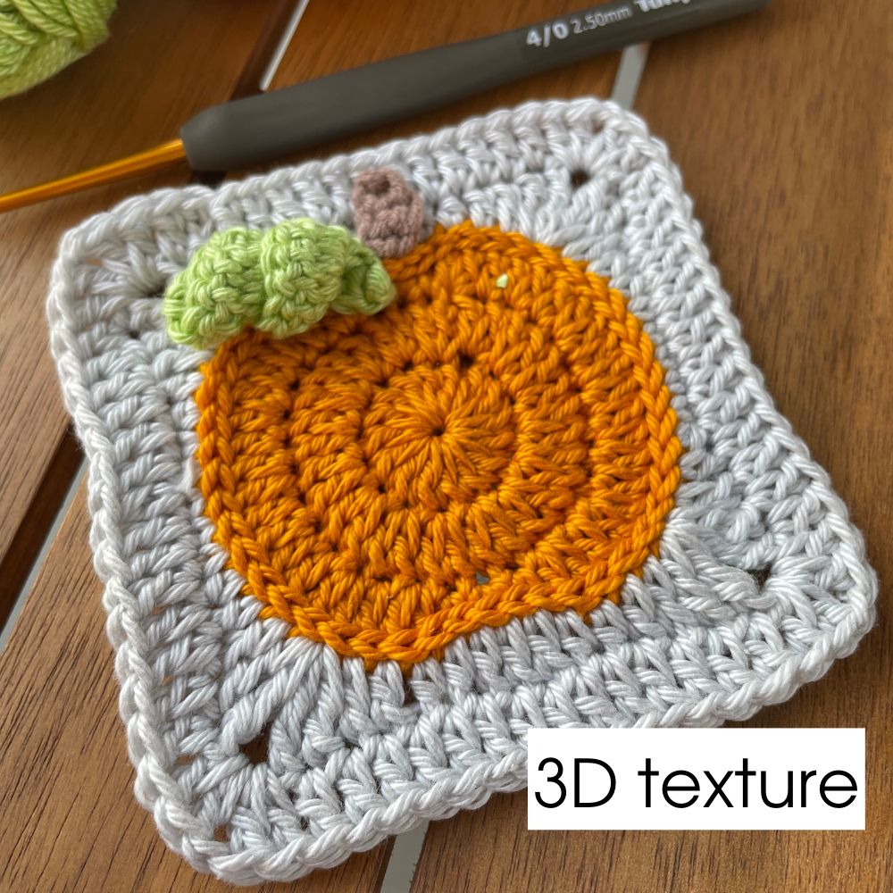 Close-up of textured crochet pumpkin square with 3D leaf detail on wooden surface