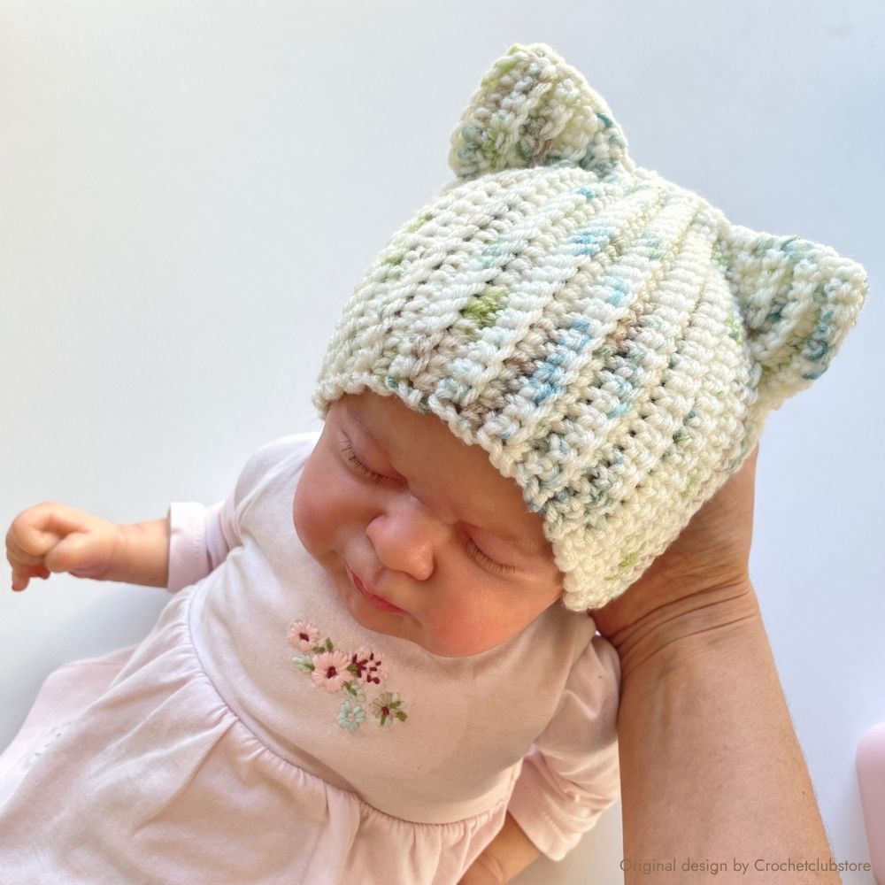 Newborn wearing handmade crochet cat ear beanie in soft speckled yarn